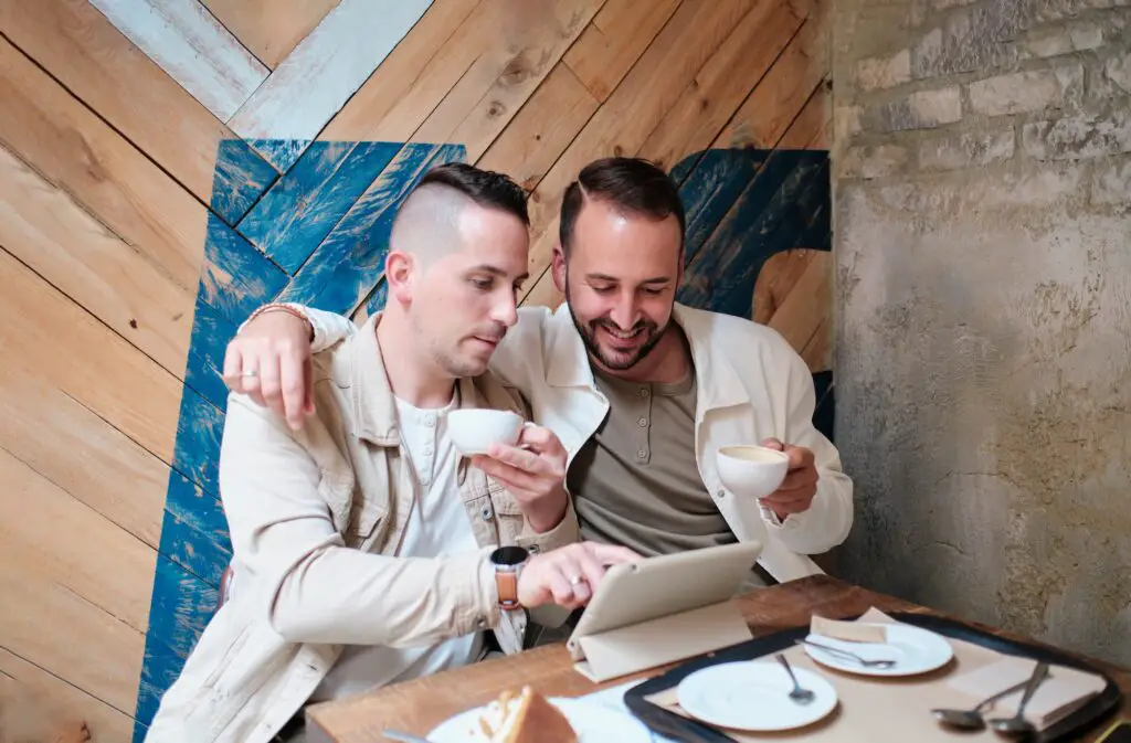 a couple of men in a coffee shop hugging using a notepad