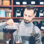 Bearded barista pouring coffee in glass