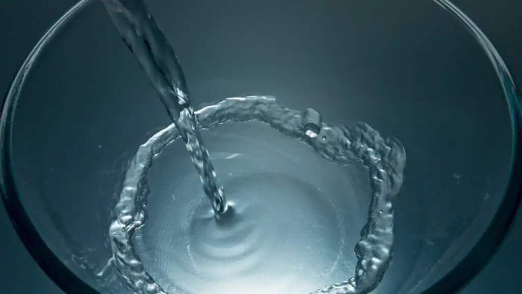 Filtered aqua jet filling glass closeup. Clear water flowing inside vessel