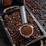 Ground Coffee in Portafilter for Espresso in a wooden tray with coffee beans.