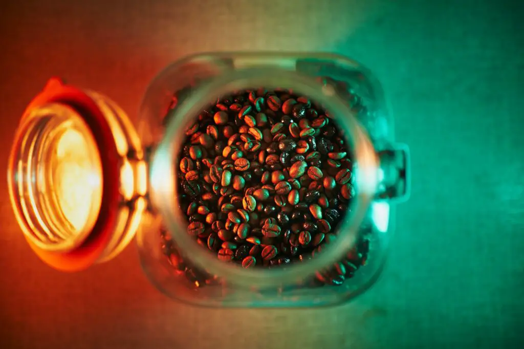 Open jar with coffee beans inside illuminated with teal and orange light