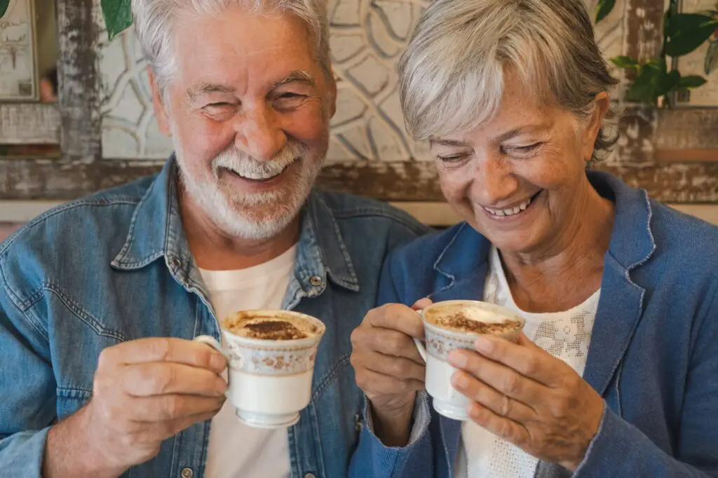 Portrait of lovely senior couple inside a coffee shop having fun and laughing while drink cappuccino