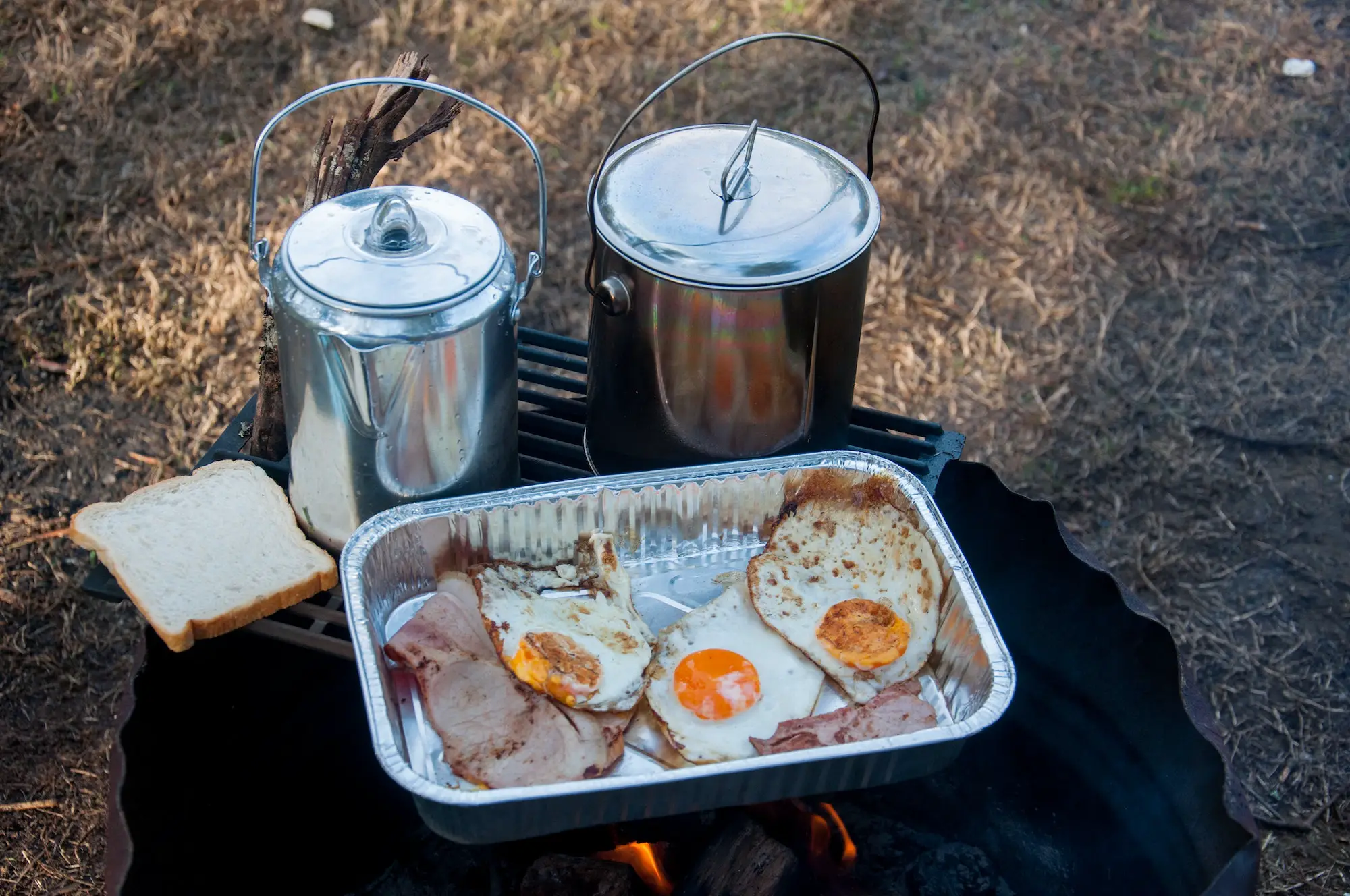 The perfect camping breakfast - bacon, eggs, bread and coffee in billy tin
