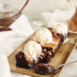 Vertical shot of delicious peanut butter swirl brownies with ice cream on top on a white table