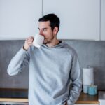 Young man with cup of coffee staying at kitchen at home