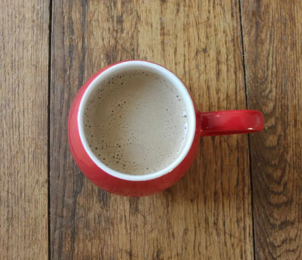 Bulletproof coffee in red mug against wooden background