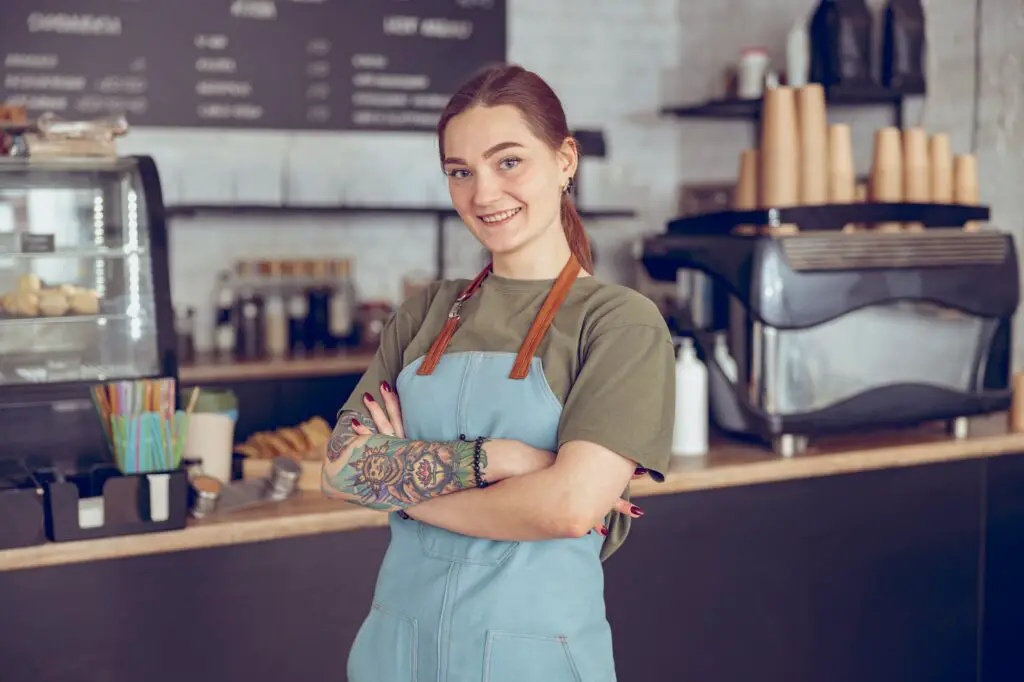Cheerful female barista in apron standing in coffeehouse