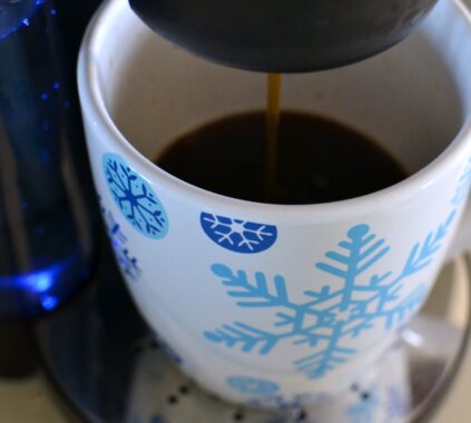 Coffee streaming into a large oversized mug with blue snowflakes from a coffee machine.