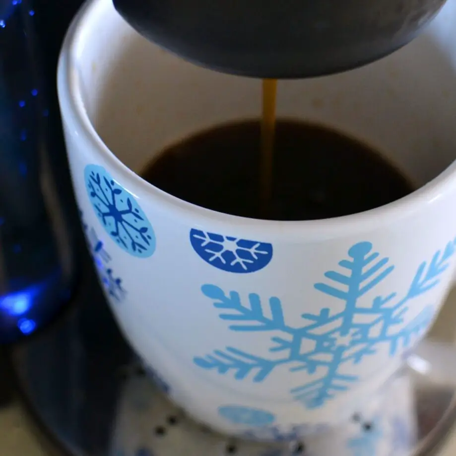Coffee streaming into a large oversized mug with blue snowflakes from a coffee machine.
