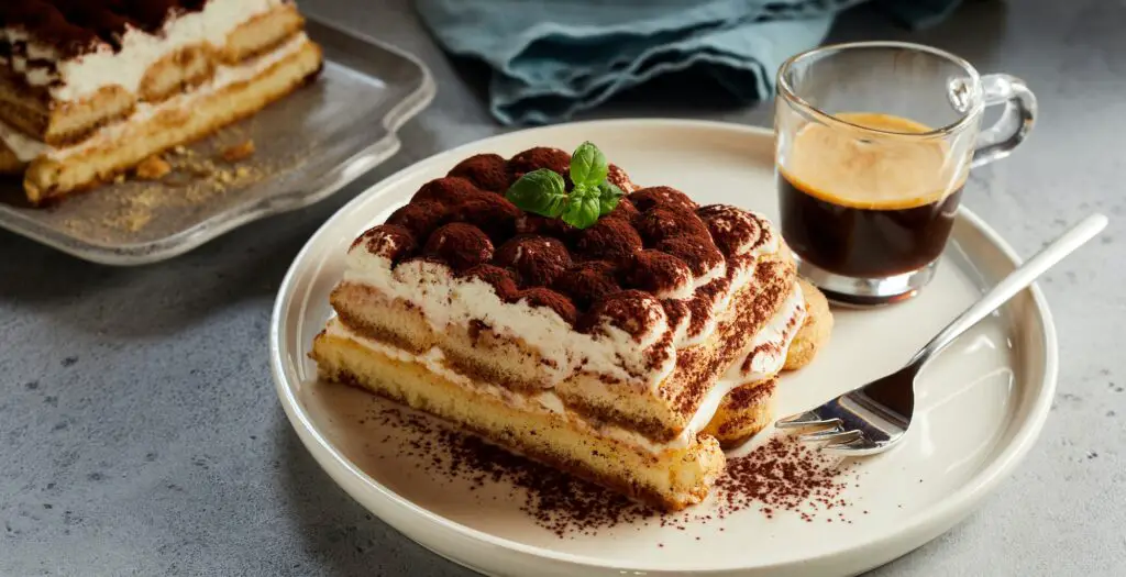 Delicious Tiramisu dessert and cup of coffee on table